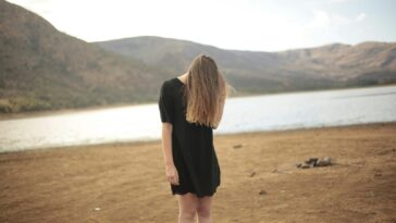 woman in black dress standing in front of lake
