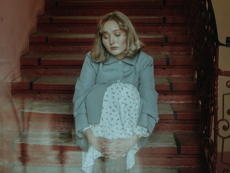 girl in pink long sleeve shirt and white skirt sitting on brown wooden staircase