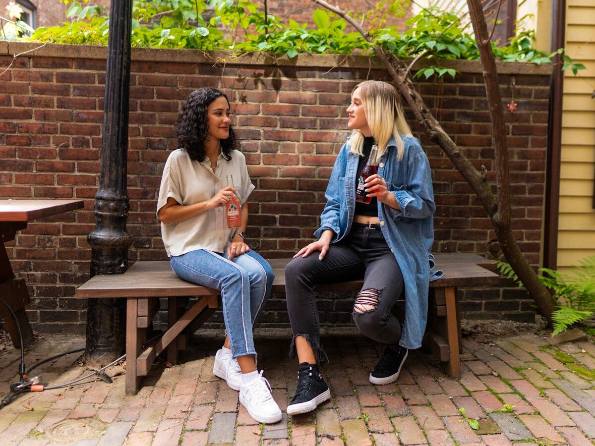 2 women sitting on brown wooden bench