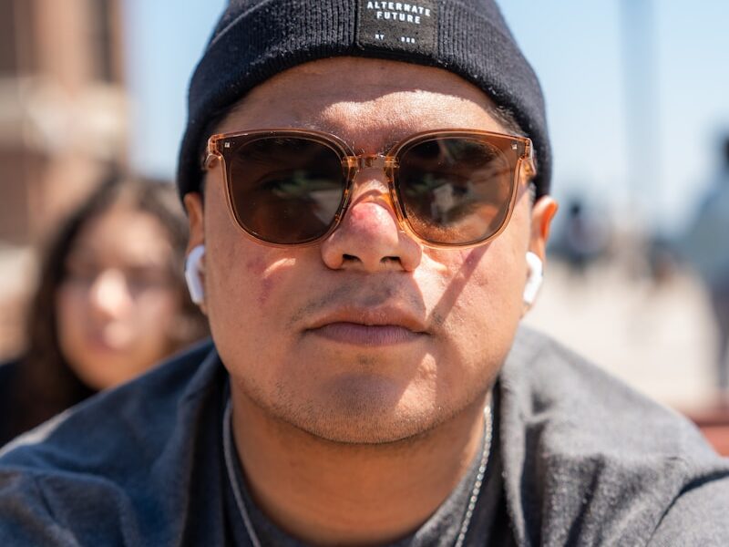 a man wearing sunglasses and a beanie looks at the camera