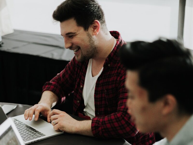 a couple of men sitting at a table with laptops
