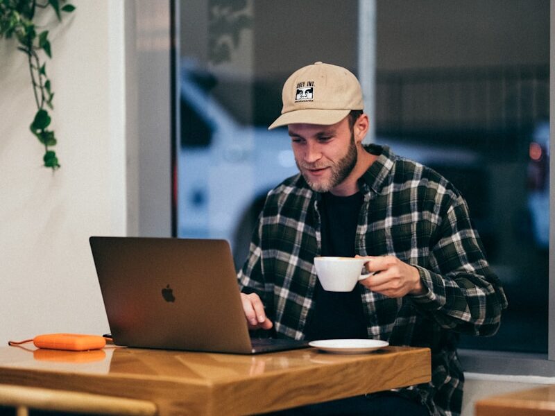 man sitting while having coffee and using laptop