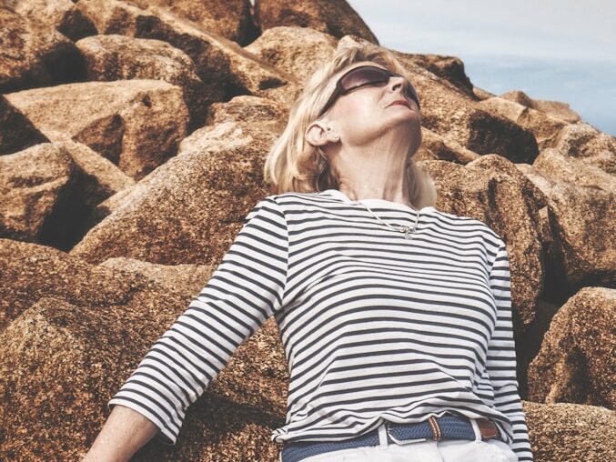 woman in black and white striped long sleeve shirt and white pants sitting on brown rock