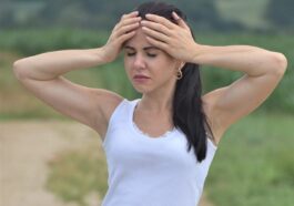 a woman in white shirt and shorts holding her hands to her head