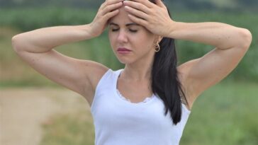 a woman in white shirt and shorts holding her hands to her head