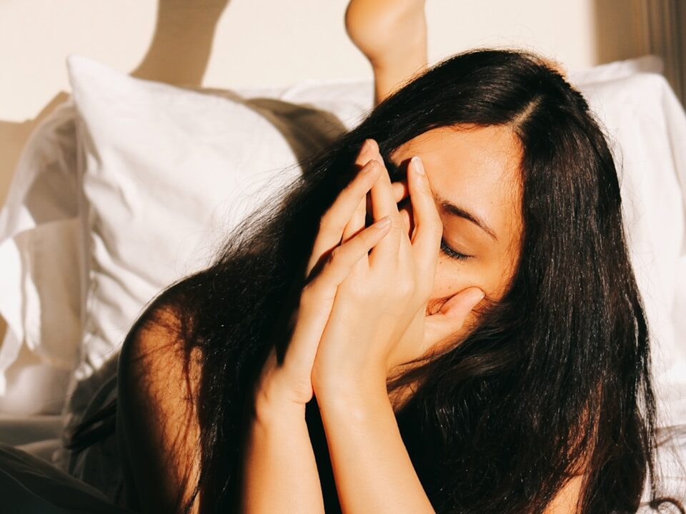 a woman laying in bed with her hands on her face
