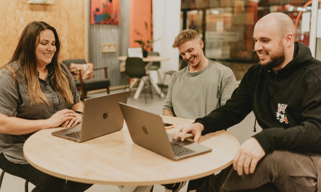 Three people collaborate around a table with laptops.