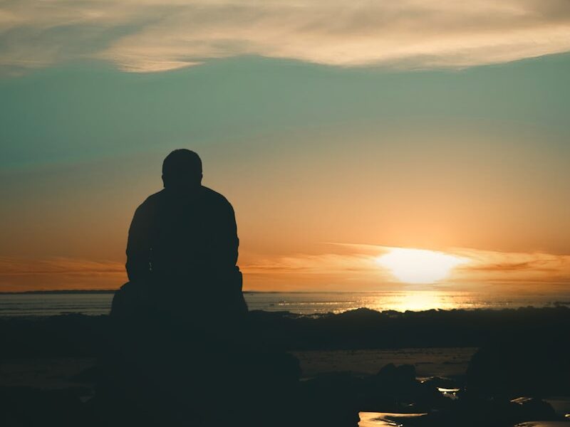 silhouette of man standing on seashore during sunset
