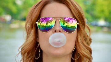 a woman wearing sunglasses blowing a bubble