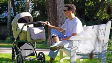a man sitting on a bench next to a baby stroller