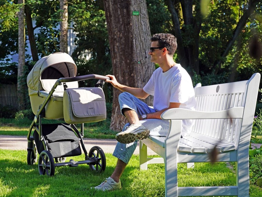 a man sitting on a bench next to a baby stroller