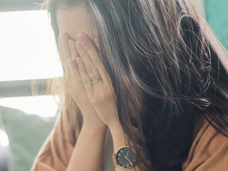 woman in brown shirt covering her face
