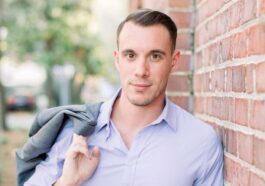 a young man leaning against a brick wall
