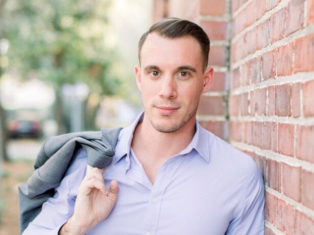 a young man leaning against a brick wall