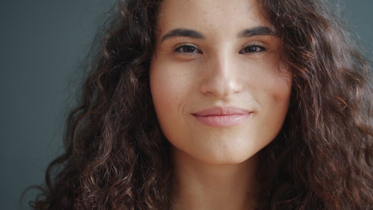 Young woman with curly hair smiles softly.