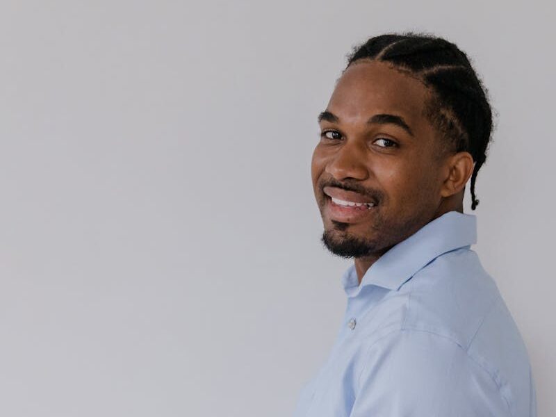 Smiling black man with braided hair in a blue shirt giving a thumbs up against a white background.