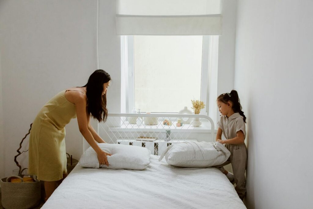 A mother and daughter making the bed together in a bright and cozy bedroom.