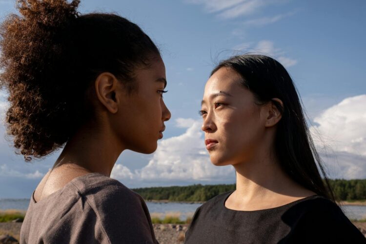 A close-up outdoor portrait of two women facing each other under a bright sky.