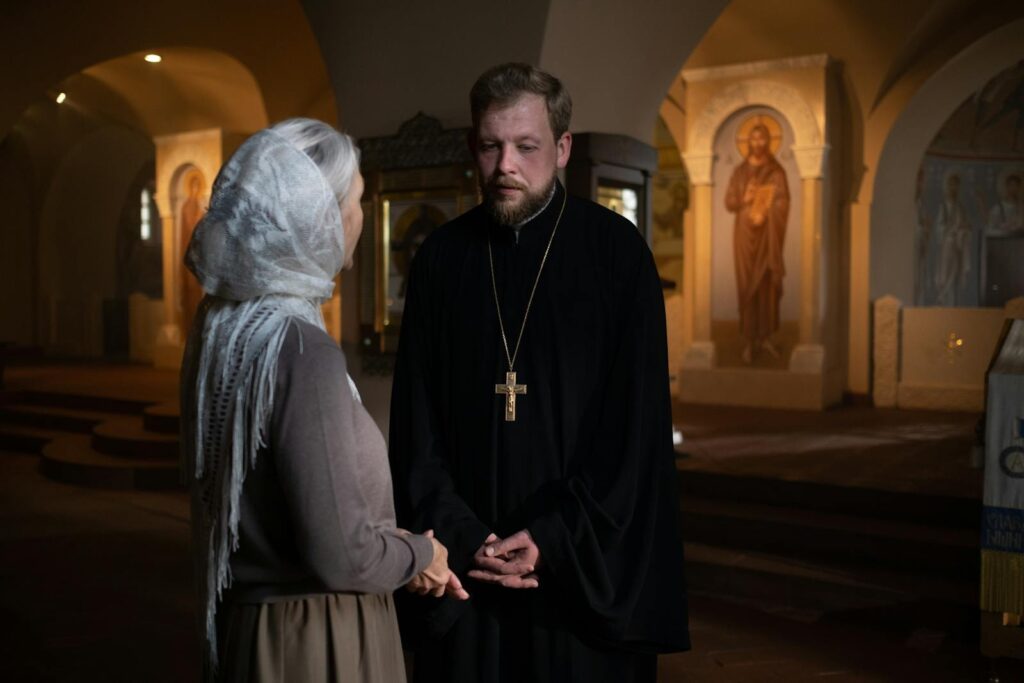 Orthodox priest and parishioner engaged in a solemn conversation inside a church.