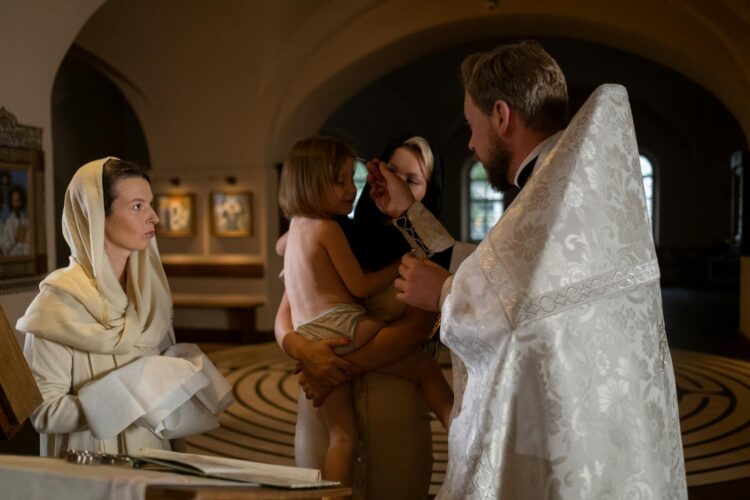 A priest conducts a baptism ceremony in a church, surrounded by family members.