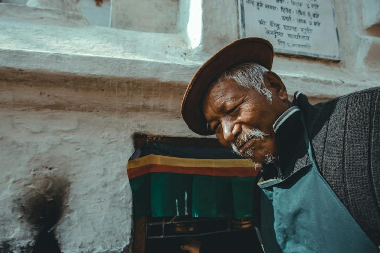 Portrait of an elderly man wearing a traditional hat next to a colorful stone wall.