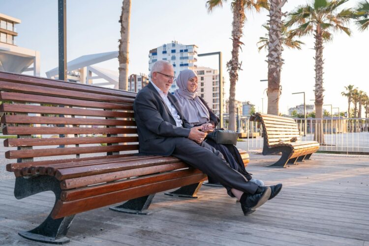 Senior couple sitting on a park bench, smiling and enjoying a peaceful sunset outdoors.
