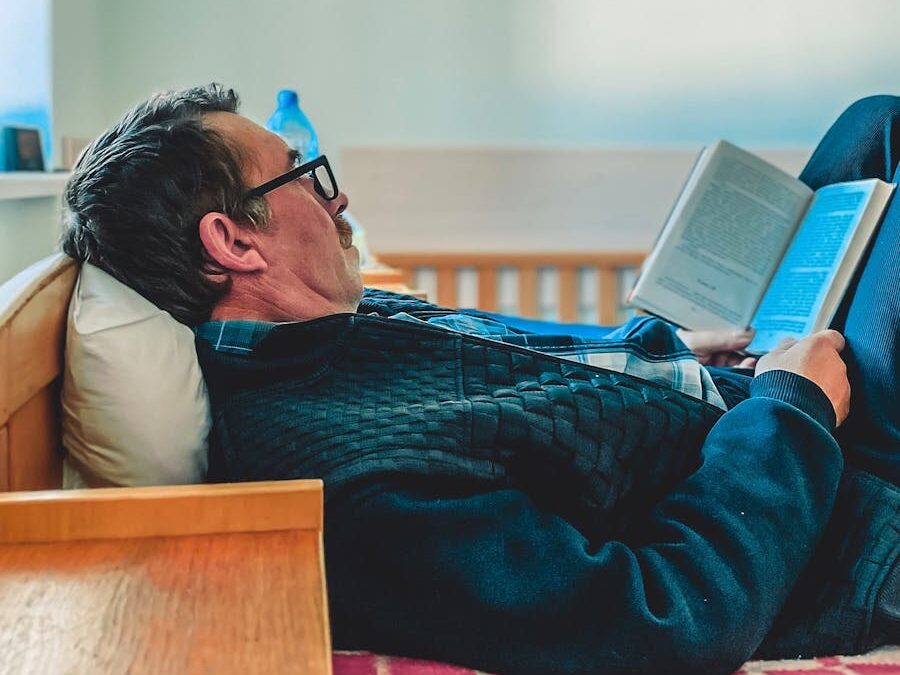 Elderly man reading a book while relaxing on a comfortable bed indoors.