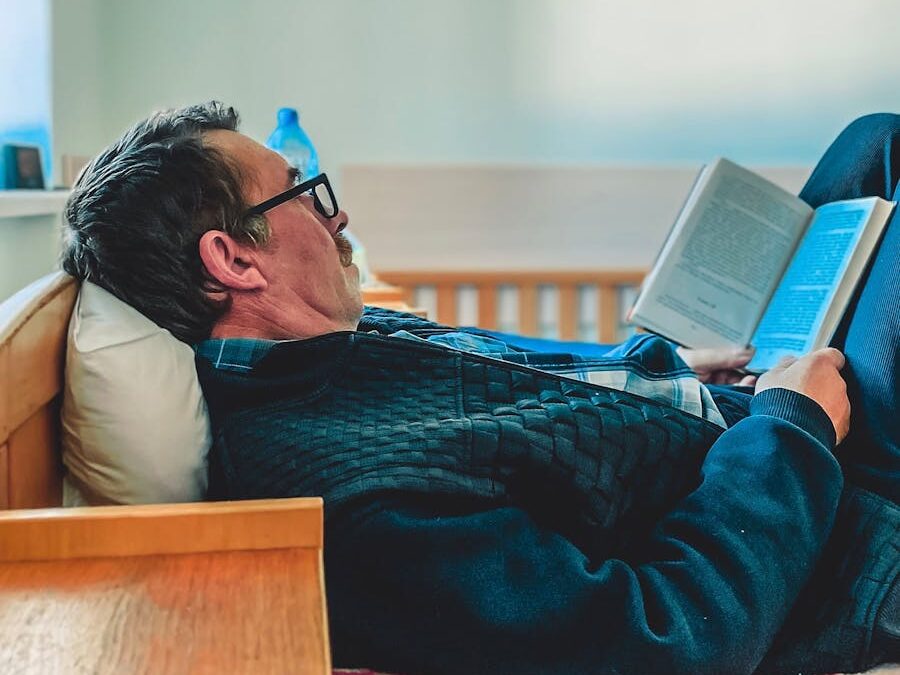 Elderly man reading a book while relaxing on a comfortable bed indoors.