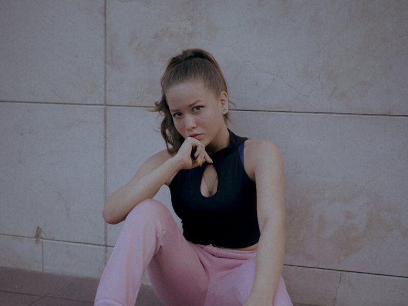 Young woman in pink pants sitting on urban floor, deep in thought.