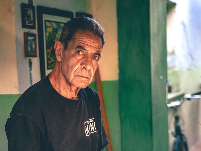 A senior man engaged in painting indoors at a wooden table, exuding a calm and artistic atmosphere.