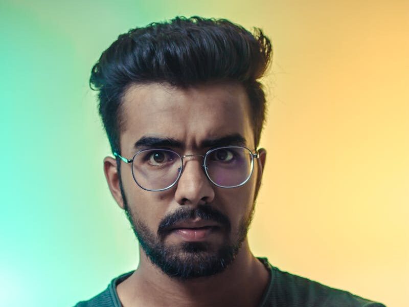 A thoughtful adult man with eyeglasses posing for a portrait with a vibrant backdrop.