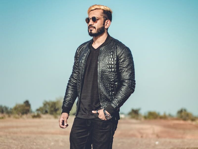 Stylish man wearing a jacket and sunglasses walks confidently outdoors.