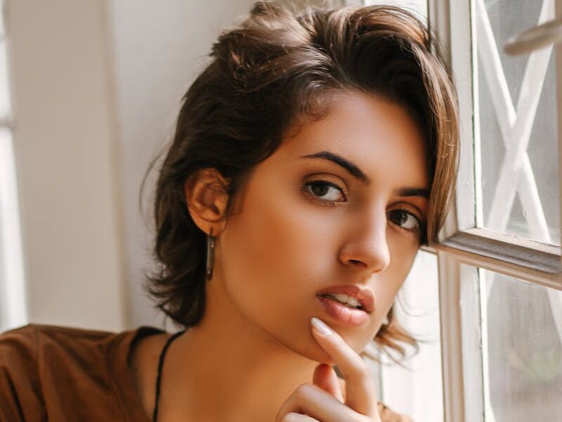 Graceful portrait of a thoughtful woman leaning against a window, capturing natural beauty and introspection.