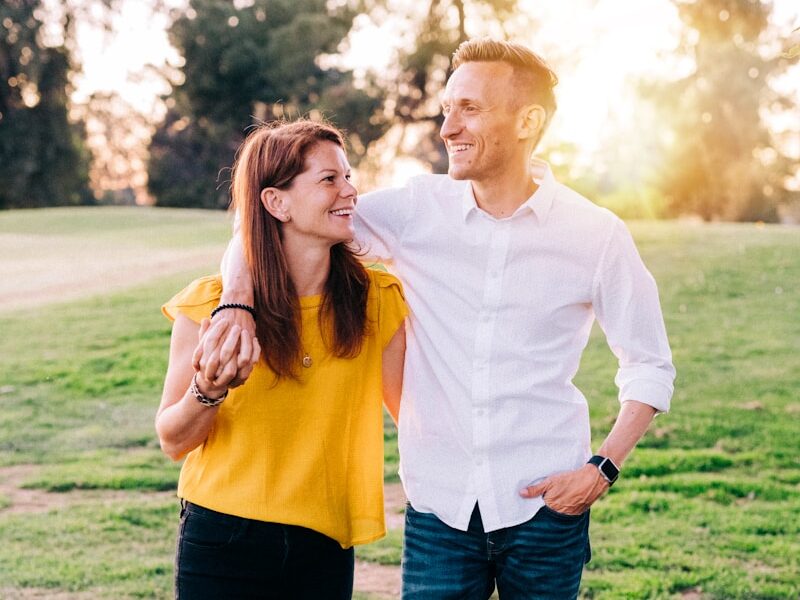 man in white dress shirt and woman in orange long sleeve shirt standing on green grass