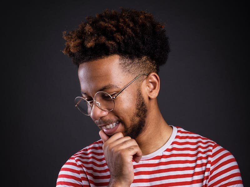 Portrait of a pensive African American man with afro and eyewear wearing a striped shirt.