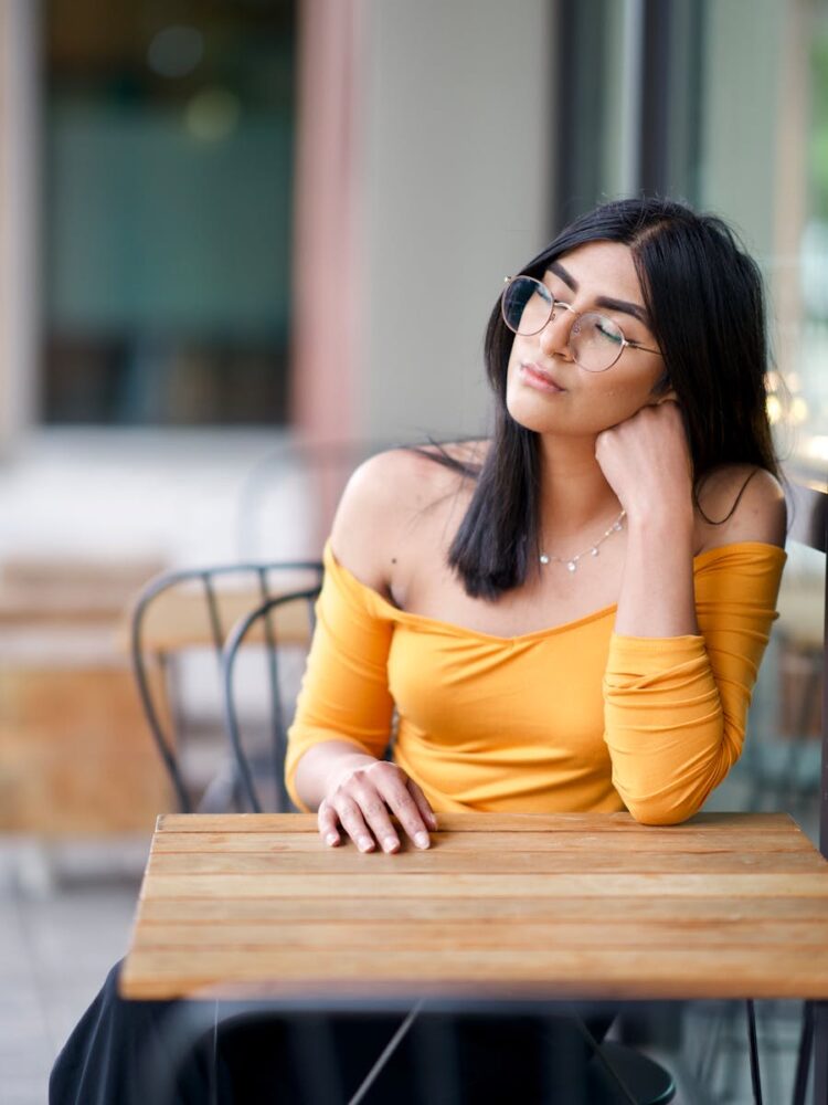 A thoughtful young woman in yellow, sitting at a table, lost in contemplation.