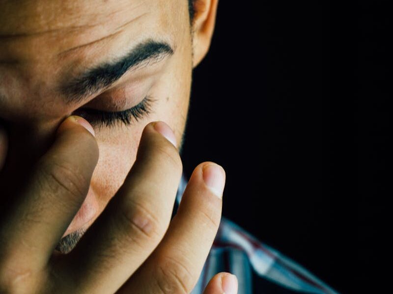 A close-up portrait capturing the emotional expression of a man in a dark studio setting.