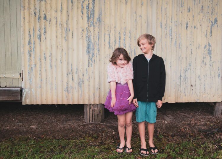 Two siblings enjoy a playful moment outdoors in Currumbin, Australia, showcasing their joyful bond against a rustic backdrop.