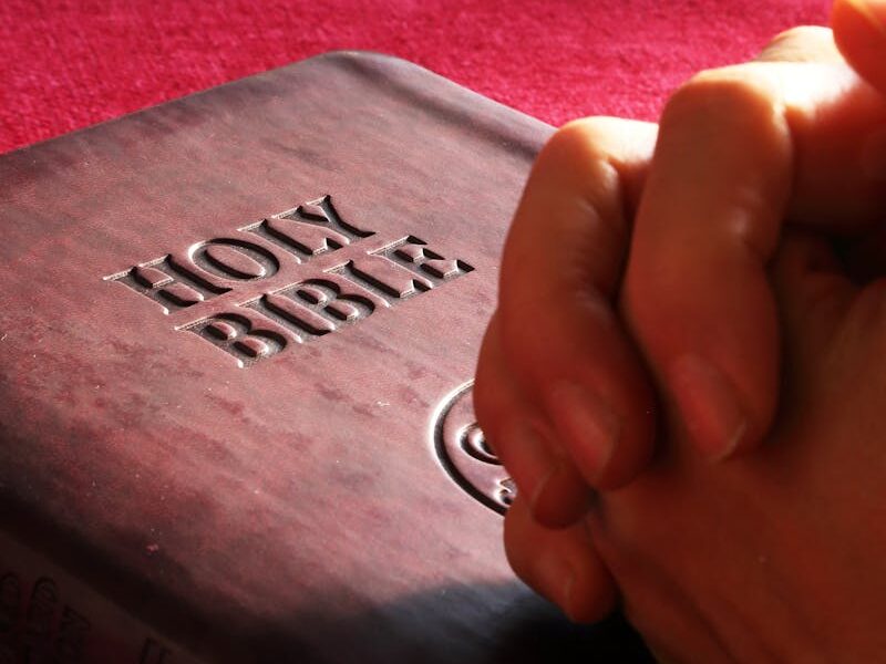 Close-up of hands praying on a Holy Bible, symbolizing faith and spirituality.