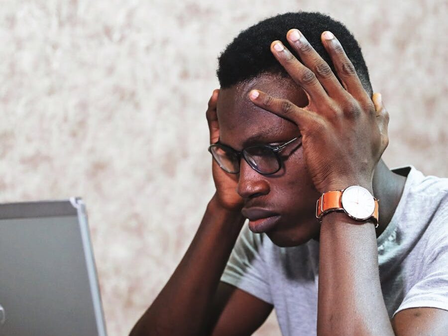 A man appears frustrated while working on a laptop in an office setting, showcasing remote work challenges.
