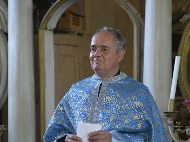 A Greek Orthodox priest in ornate blue robes inside a historic church.