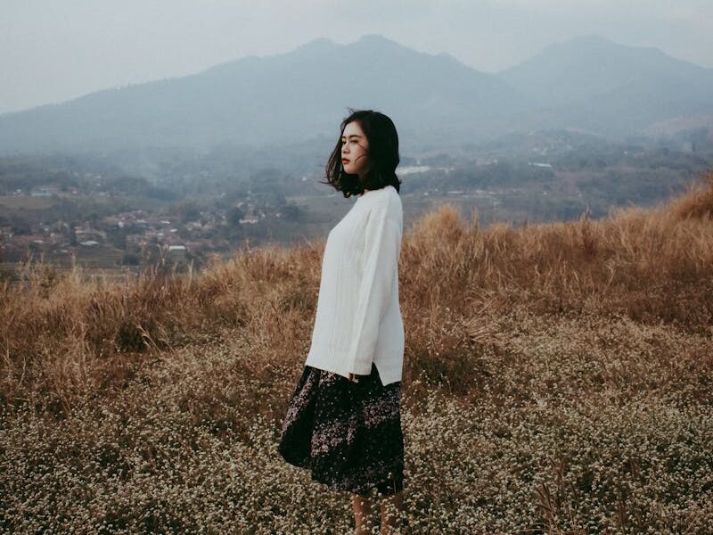 Woman standing in a serene meadow, Bandung, Indonesia, with mountains in the background.
