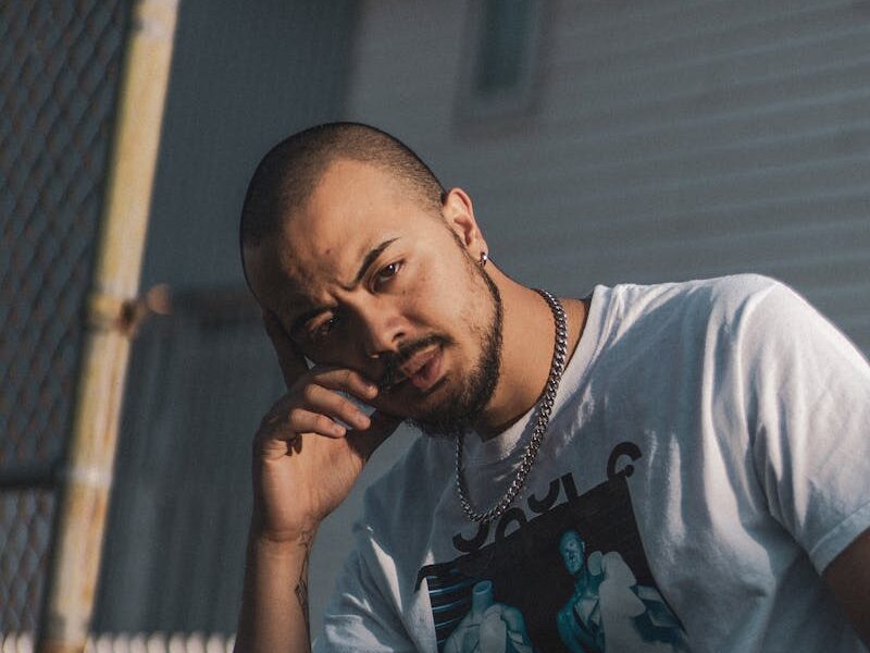 Portrait of a man outdoors in an urban setting, showcasing a pensive expression and fashion style.