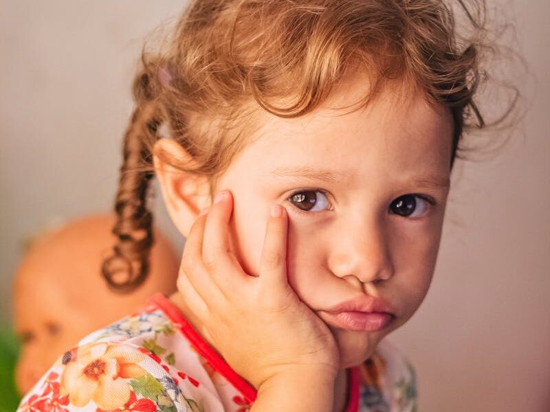 Charming portrait of a thoughtful toddler in a colorful floral dress indoors.