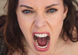 Close-up of a woman with blue eyes expressing intense emotion through a scream.