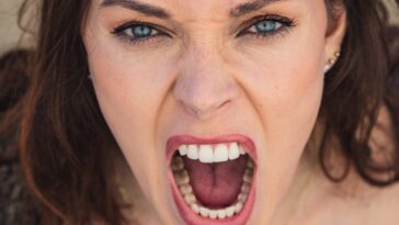 Close-up of a woman with blue eyes expressing intense emotion through a scream.