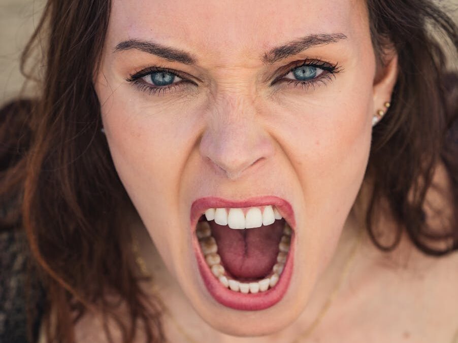 Close-up of a woman with blue eyes expressing intense emotion through a scream.