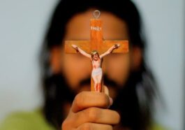 A person holding a crucifix and wearing beaded bracelet.