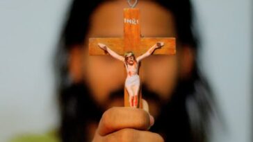 A person holding a crucifix and wearing beaded bracelet.