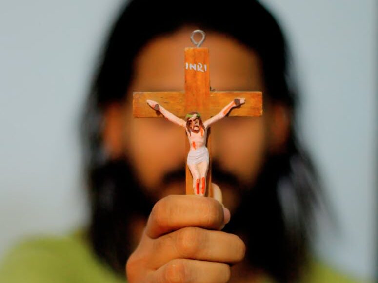 A person holding a crucifix and wearing beaded bracelet.